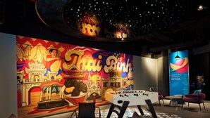 Una habitación con un amplio mural de arquitectura tailandesa, una mesa de fútbol de mesa y asientos modernos.