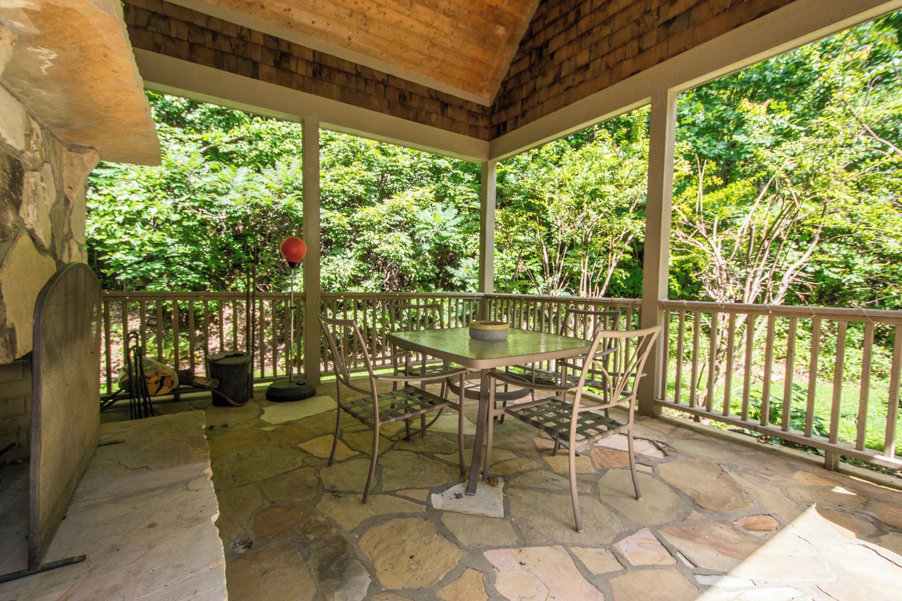 A covered patio with a stone floor, a table with chairs, and a view of a lush green garden.