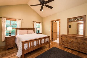 Quarto com cama de madeira, mesas de cabeceira, cômoda, espelho e ventilador de teto.