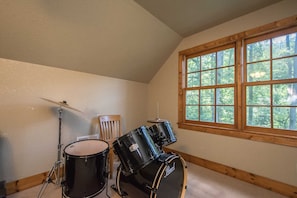 A room with a sloped ceiling, a large window with a view of trees, and two black Pearl drums.