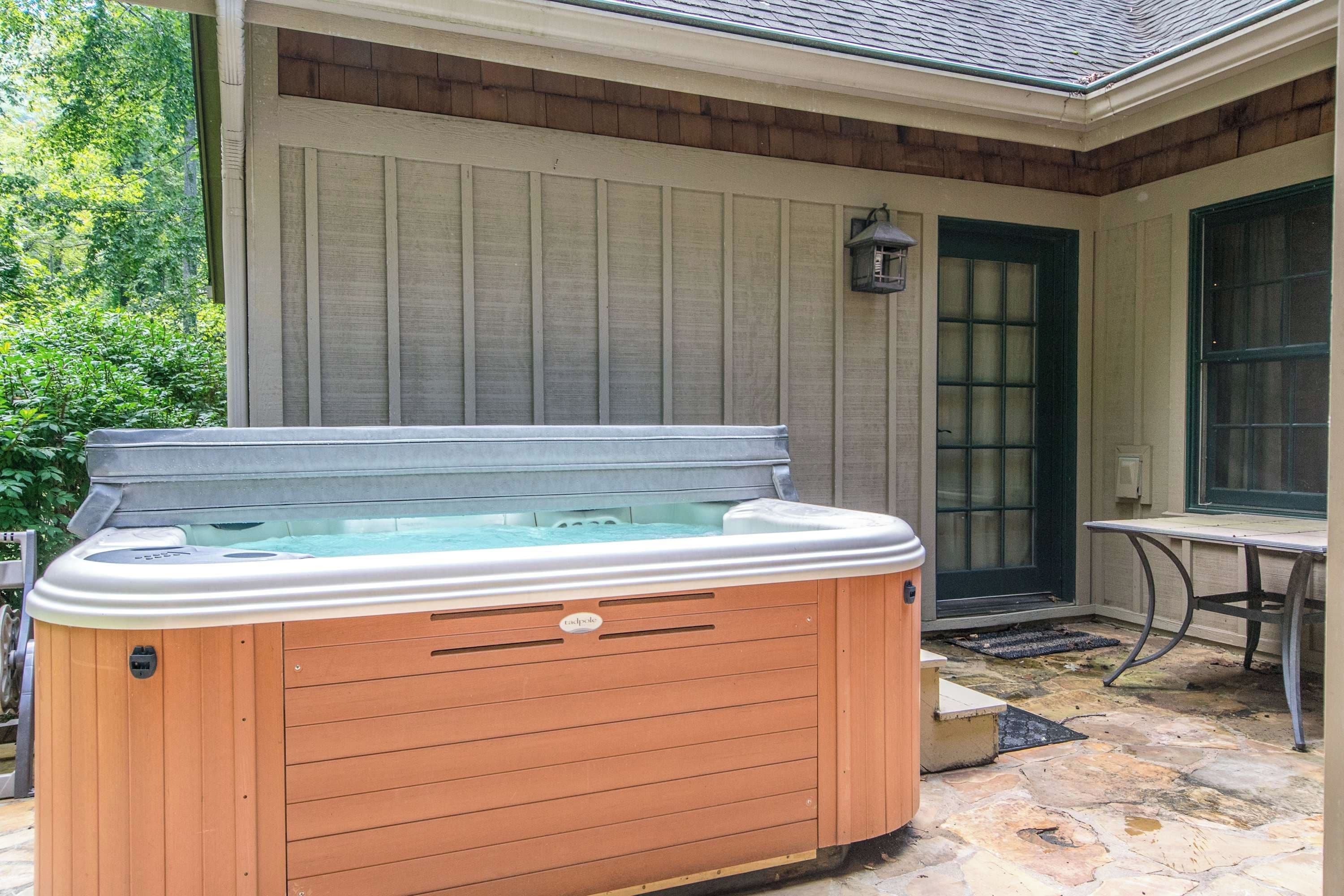A hot tub in front of a house with a wooden exterior and a stone patio.