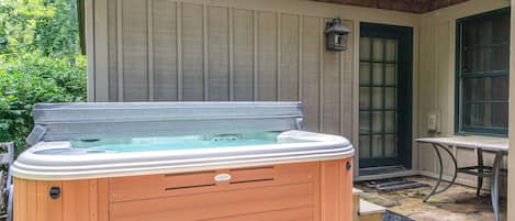 A hot tub in front of a house with a wooden exterior and a stone patio.