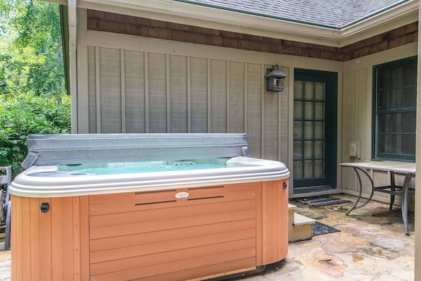 A hot tub in front of a house with a wooden exterior and a stone patio.