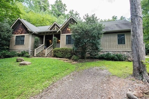 A two-story house with a front porch, a stone staircase, and a gravel driveway.