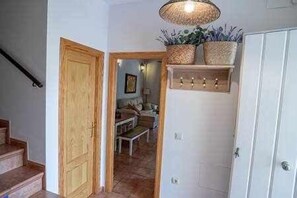 A hallway with a wooden door, a staircase, and a white wall with a shelf holding plants.