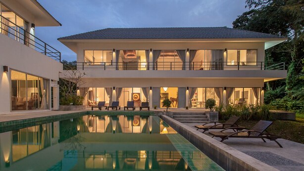 Una casa moderna de dos pisos con piscina, mobiliario exterior y un interior bien iluminado.