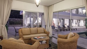 Una sala moderna con un sofá, dos sillas de mimbre, una mesa de centro y un ventanal que da a un área exterior con sillones y una piscina.
