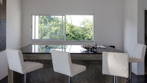 Una cocina moderna con un amplio ventanal, una mesa de cristal y tres sillas blancas.