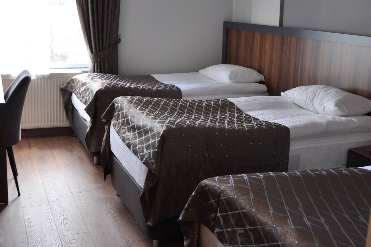 A hotel room with two beds, a chair, and a window with curtains.