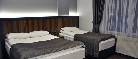 Habitación de hotel con dos camas, cabecero de madera, un ventanal con cortinas translúcidas y una mesita de noche.