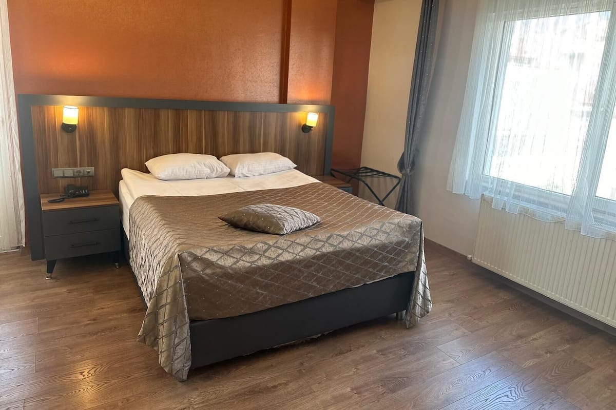 A hotel room with a bed, bedside tables, a lamp, a chair, and a window with curtains.