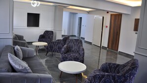 A modern lobby with a grey sofa, patterned armchairs, a round table, and a wooden door. - Saka Life Hotel (Erzurum)