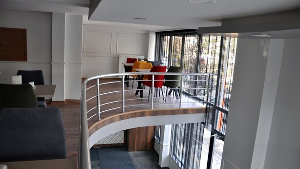 A modern hotel lobby with a curved staircase leading to a balcony with red and yellow chairs. - Saka Life Hotel (Erzurum)
