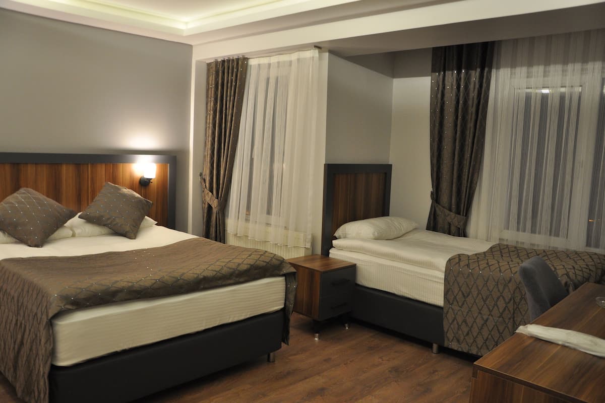 A hotel room with two beds, a wooden nightstand, a desk, and a mirror.
