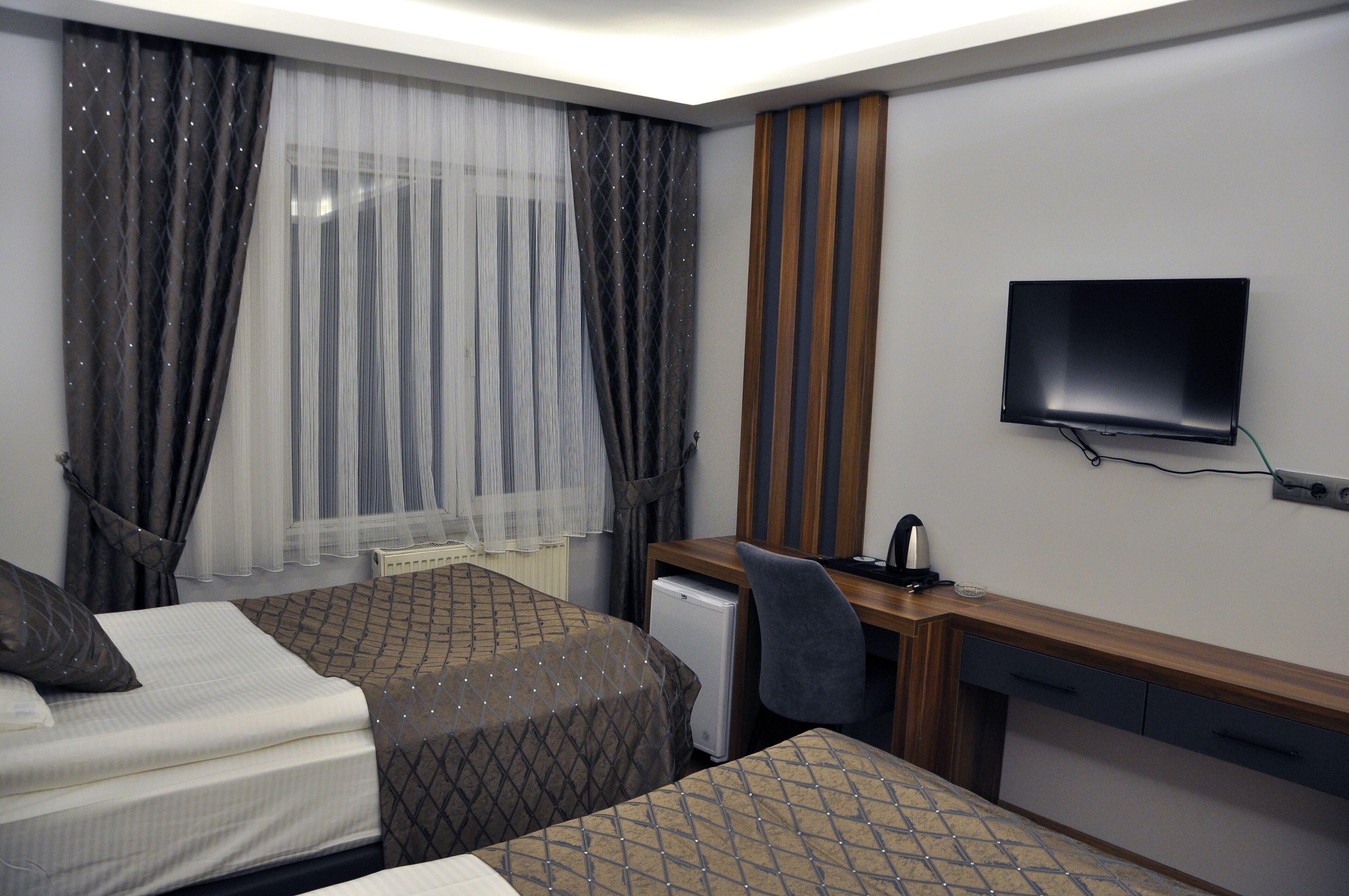 Quarto de hotel com duas camas, uma escrivaninha, uma cadeira, uma televisão e uma janela com cortinas.