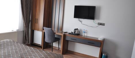 Une chambre d’hôtel comprenant un lit, un bureau, une chaise, une télévision, un radiateur, une armoire et une poubelle.