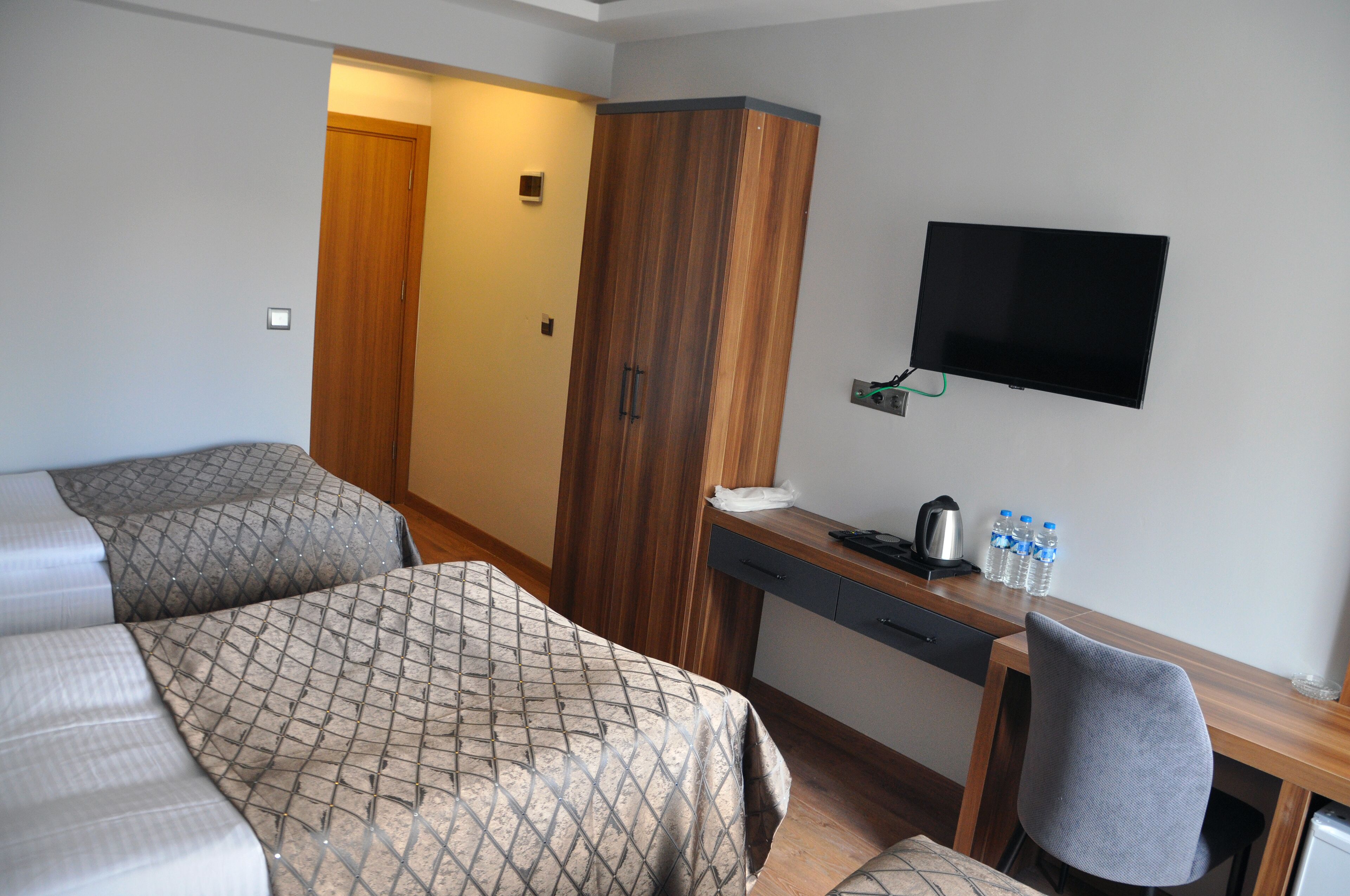 A hotel room with two beds, a wooden wardrobe, a desk with a chair, a flat-screen TV, and a coffee maker.