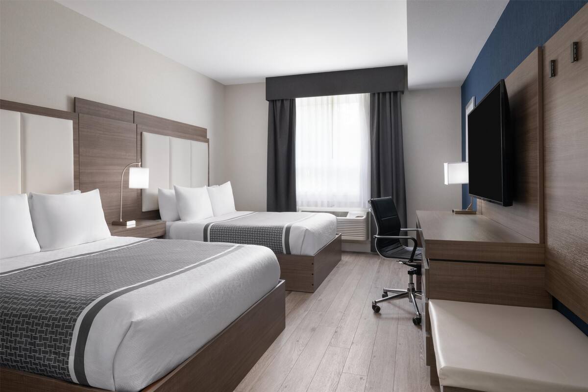 Une chambre d’hôtel avec deux lits, un bureau, une chaise, une télévision et une fenêtre avec des rideaux.