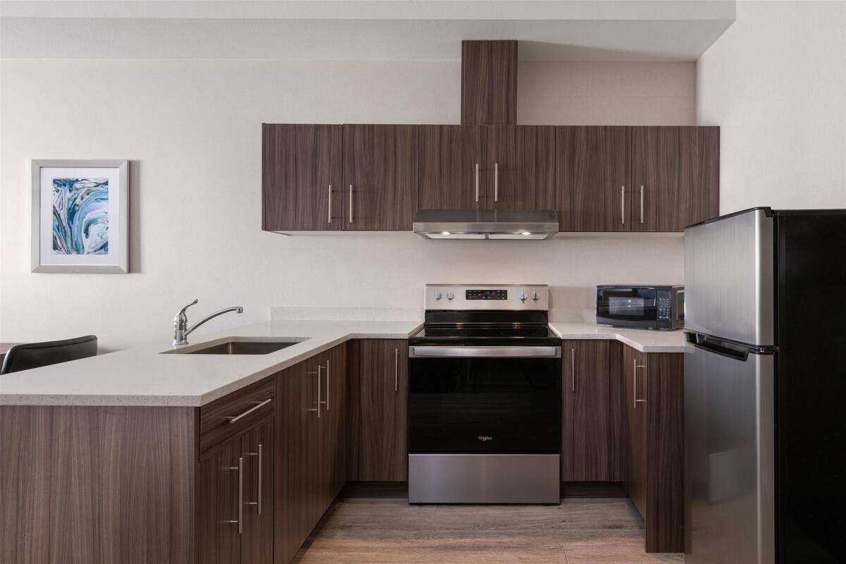 Une cuisine moderne avec des meubles en bois foncé, des appareils électroménagers en acier inoxydable et un plan de travail blanc.