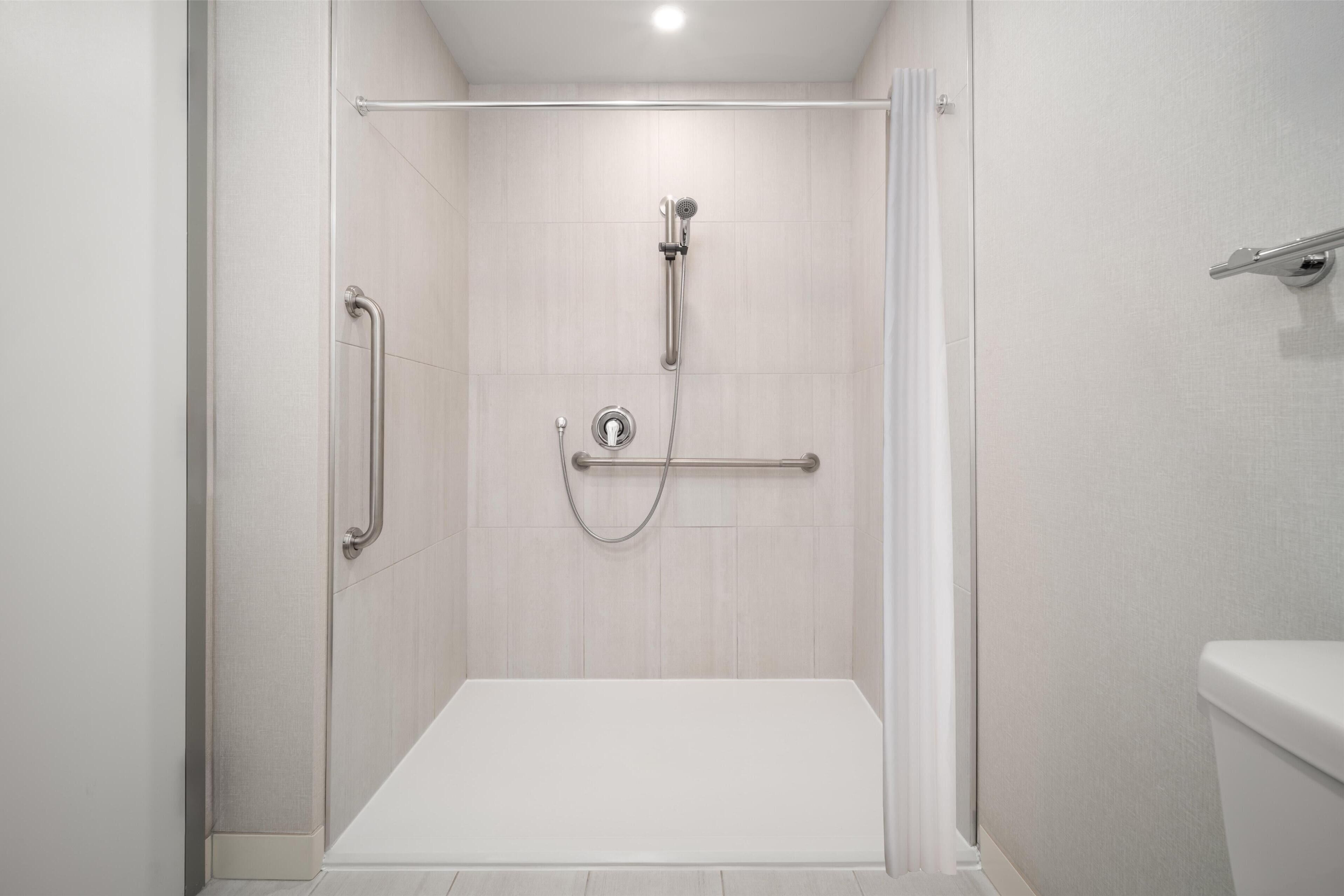A modern shower area with a grab bar, a handheld showerhead, and a control panel.