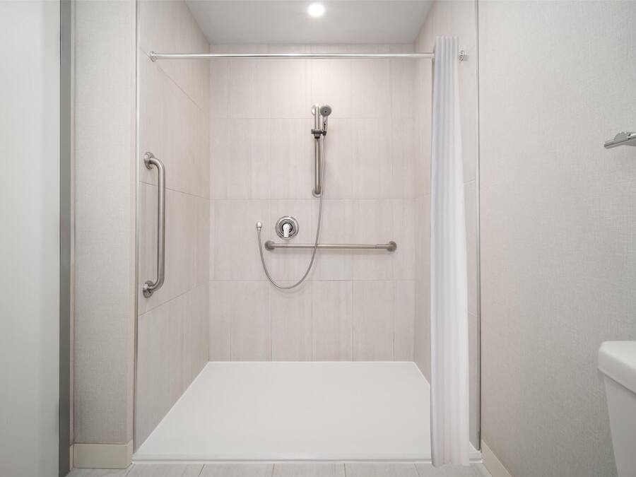 A modern shower area with a grab bar, a handheld showerhead, and a control panel.