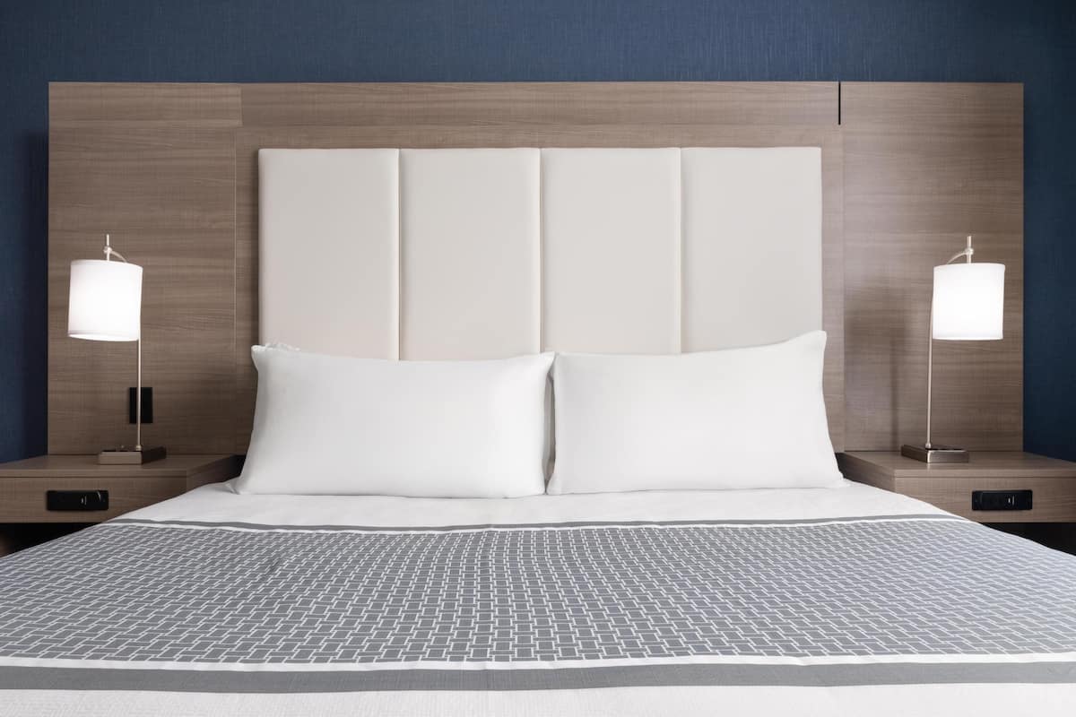 Un lit bien fait, recouvert d’une couvre-lit à motifs, avec deux tables de chevet dotées de lampes et une tête de lit en bois.