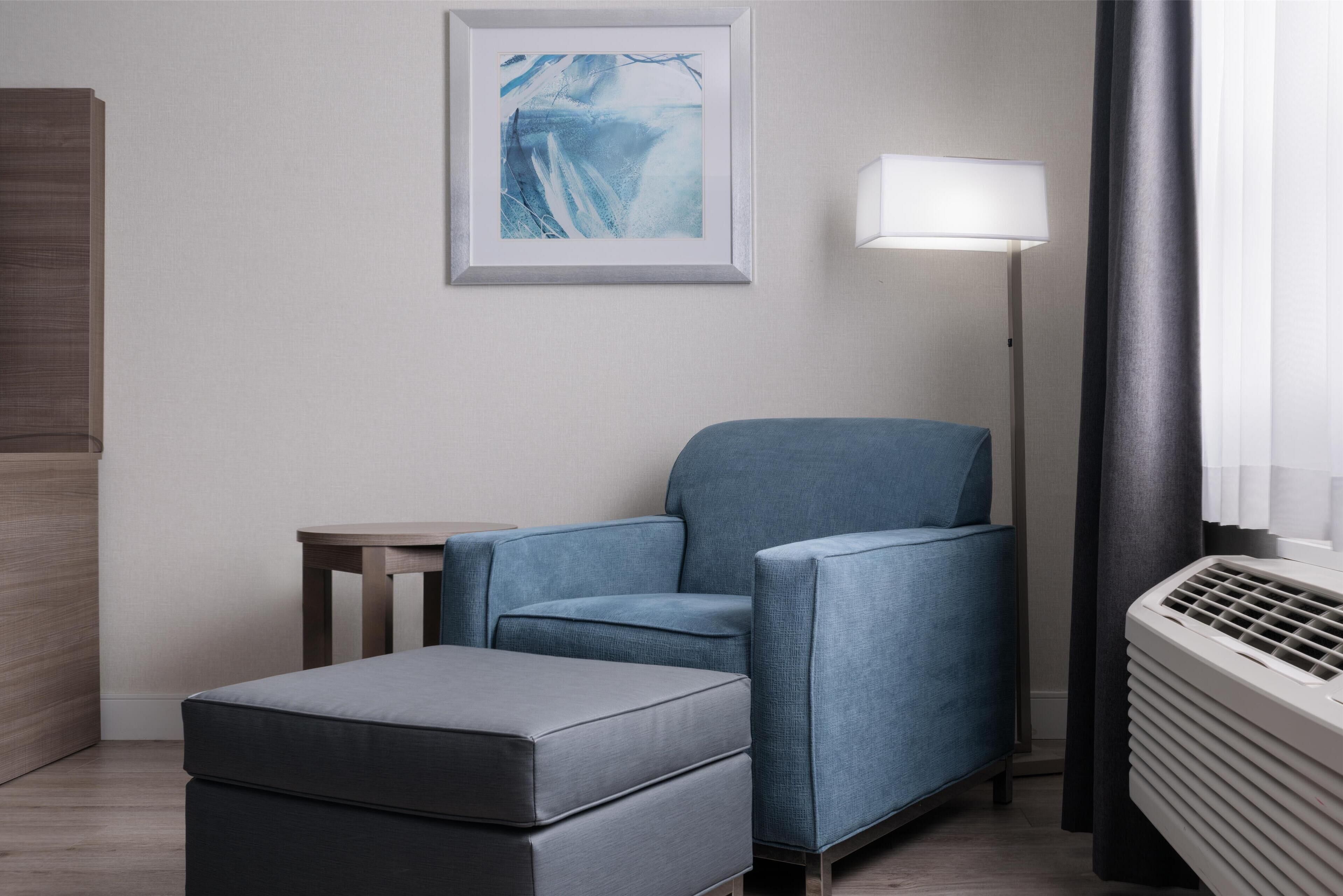 A modern hotel room with a grey sofa, a small table, and a framed artwork on the wall.
