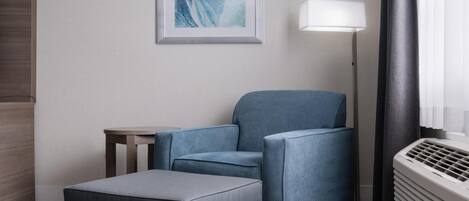 A modern hotel room with a grey sofa, a small table, and a framed artwork on the wall.