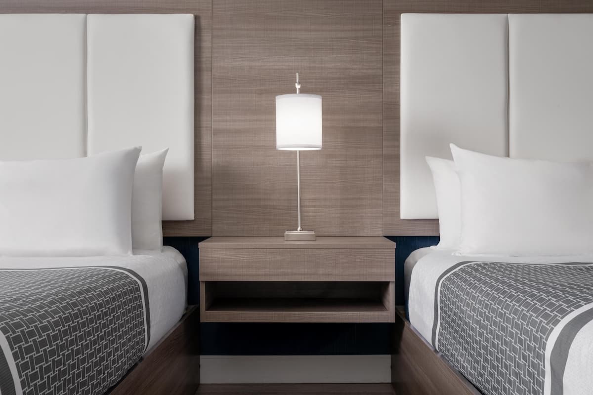 Une chambre d’hôtel moderne avec deux lits, une table de chevet avec une lampe et une étagère intégrée.