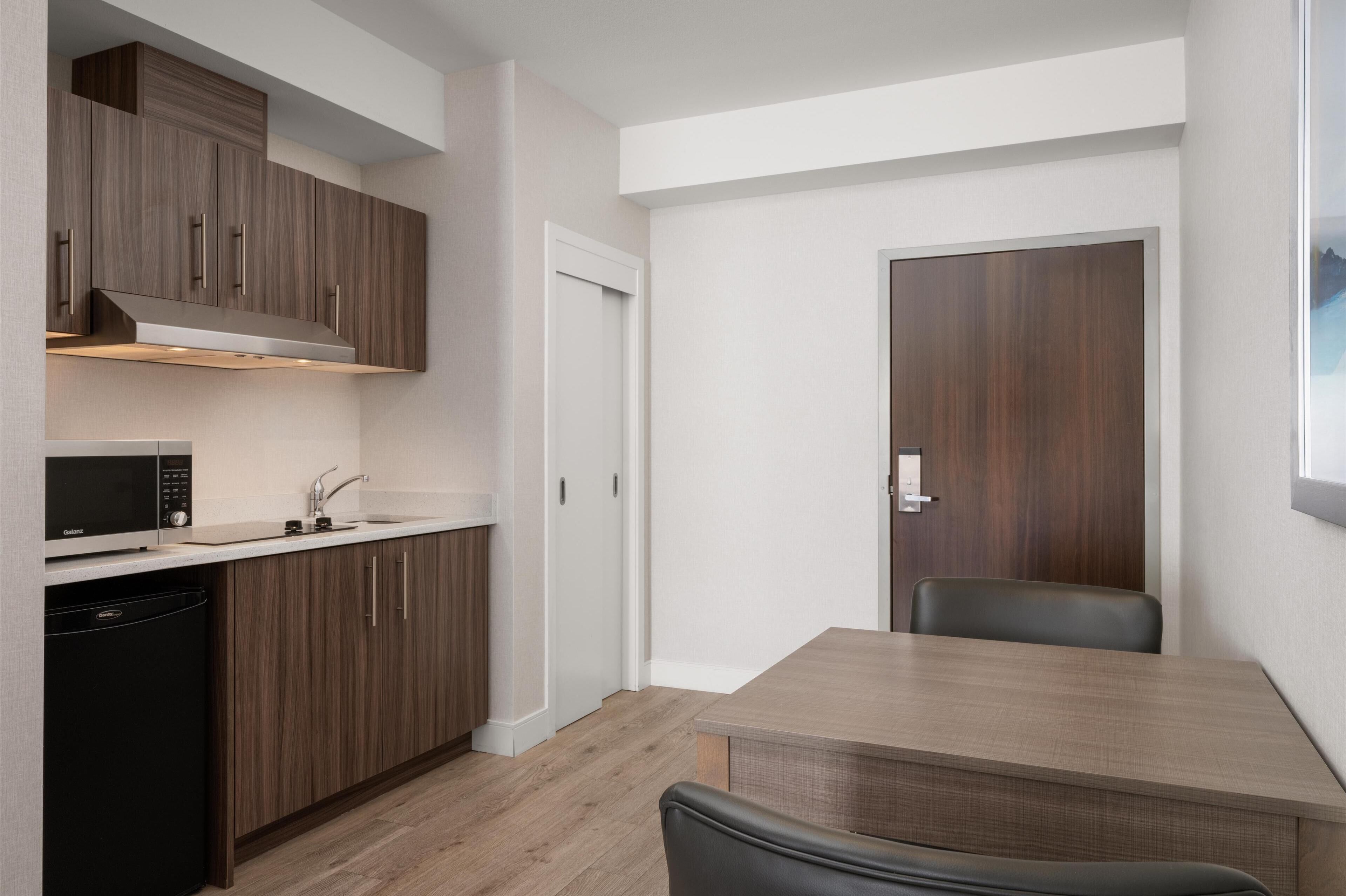 A compact kitchen with modern appliances, a dining area with a table and chairs, and a wooden door.