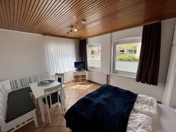 Une chambre d’hôtel avec un lit, un bureau avec un ordinateur, une chaise et une fenêtre avec des rideaux.