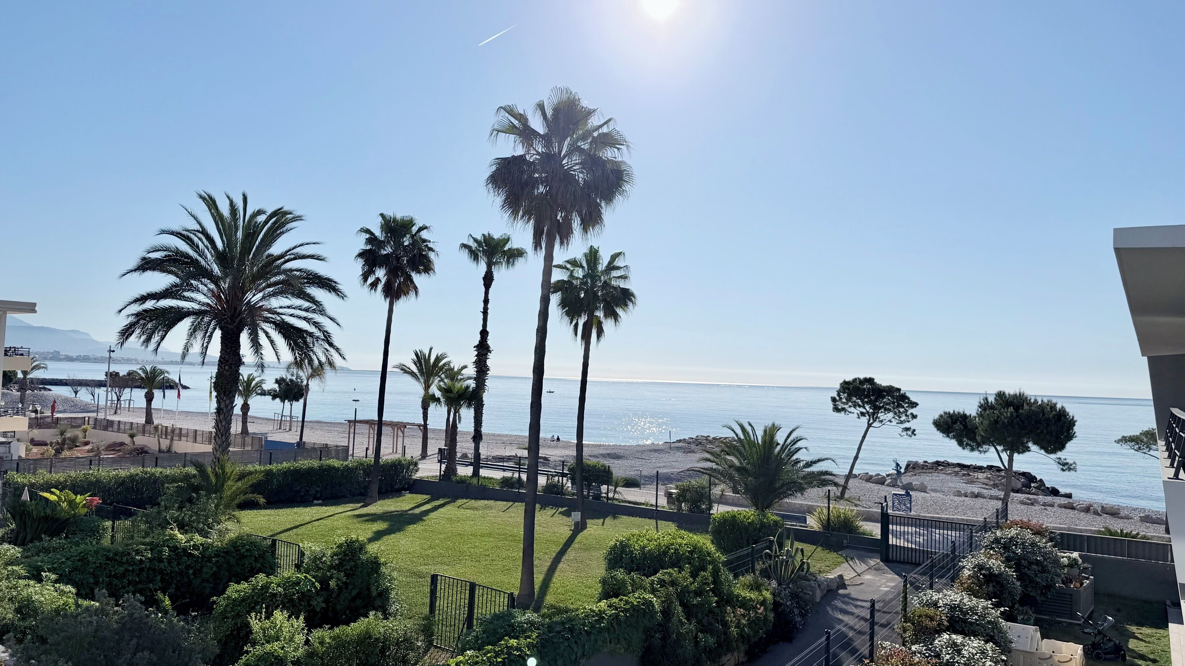 Blick auf einen Strand mit Palmen, einem klaren Himmel und einem fernen Gebirge.