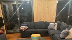 Una sala de estar con un sofá seccional gris, un otomanillo redondo y un tapete gris sobre el piso de madera.