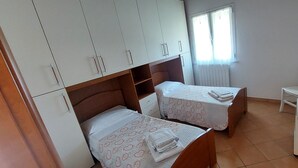 Un dormitorio con dos camas individuales, una silla, un escritorio y un armario.