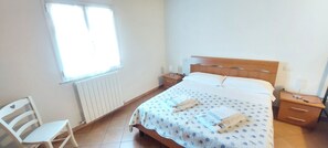 A bedroom with a bed, a chair, a bedside table, and a window.
