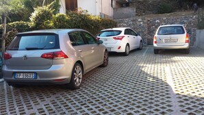 Tres coches aparcados en una entrada con un muro de piedra y vegetación al fondo.