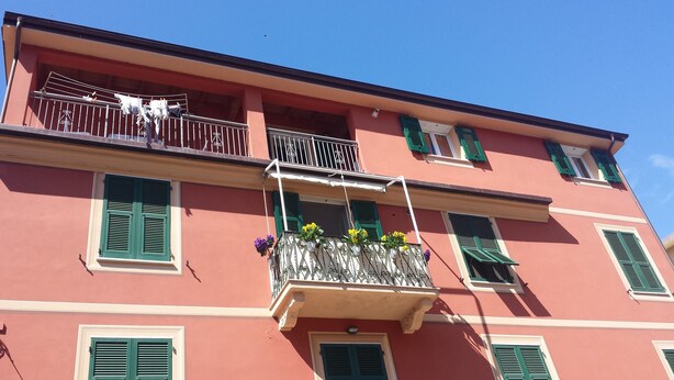 Un edificio con balcones, contraventanas verdes y jardineras con flores.