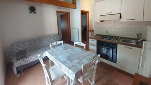 Cocina compacta con gabinetes blancos, estufa a gas y pileta. Una mesa de comedor con sillas se ubica frente a un sofá.