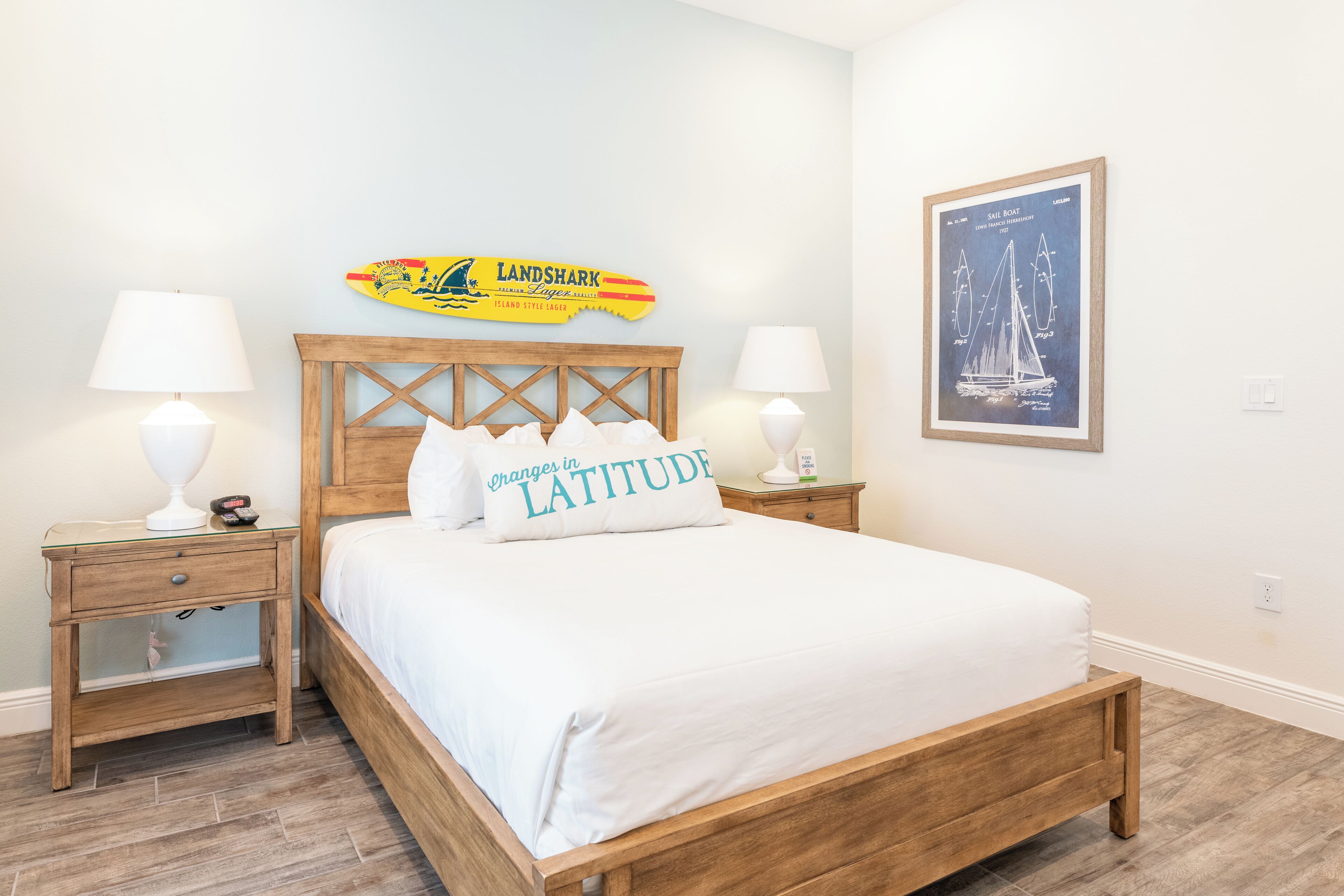 A neatly arranged bedroom with a wooden bed, two bedside tables with lamps, a wall-mounted artwork, and a decorative sign above the bed.