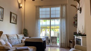 A living room with a sofa, a small table, and a fireplace. There is a large window with curtains and a view of the outside. - Casa el Paraíso del Lago Rural Lodging (AN)