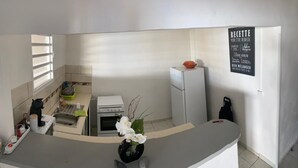 Eine kompakte Küche mit Kühlschrank, Backofen und Spüle. Ein kleines Fenster und eine an der Wand befestigte Rezepttafel sind vorhanden.