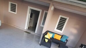 Ein großzügiger Patio-Bereich mit gefliestem Boden, einer Couch mit Kissen und einer Tür zu einem Innenraum.