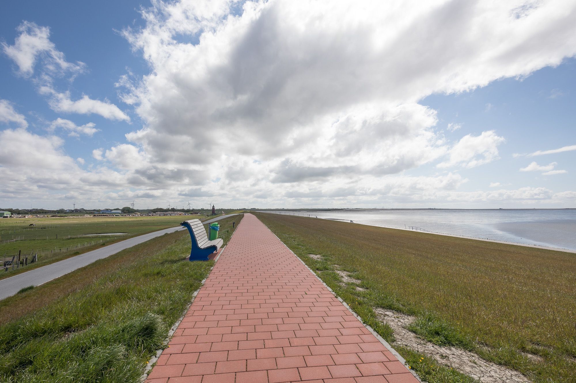 Un chemin pavé longe une zone côtière, avec des berges verdoyantes et un ciel dégagé.