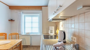 A kitchen with a wooden table, chairs, a sink, a window with curtains, and a tiled backsplash. - Guesthouse Am Badedeich, vacation apartment Sylt in Dagebüll for up to 4 people (Dagebüll)