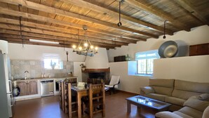 A spacious living area with a wooden ceiling, a dining table with chairs, a sofa, and a fireplace.