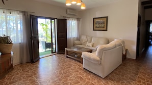 A living room with a sofa, a coffee table, a potted plant, and a sliding glass door leading to an outdoor area.