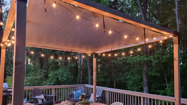 Eine Terrasse im Freien mit Holztisch und -stühlen, Lichterketten und einer Pergola.