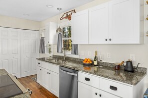 A modern kitchen with white cabinets, granite countertops, a stainless steel dishwasher, and a built-in oven.