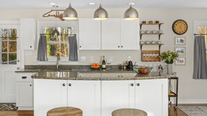 Eine moderne Küche mit weißen Schränken, einer Granit Arbeitsplatte und drei Pendelleuchten.
