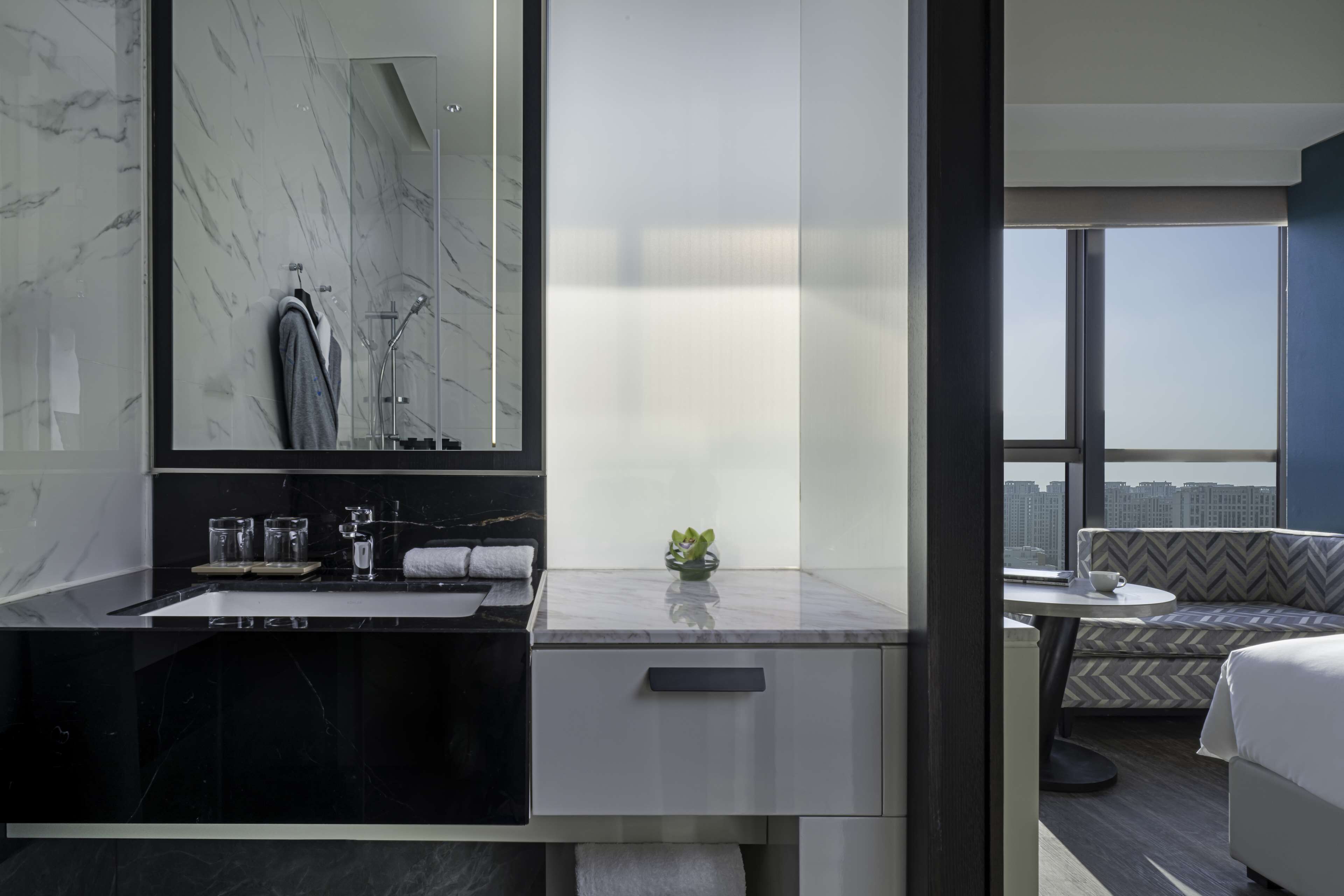 Un baño moderno con un espejo grande, encimera de mármol negro y una pequeña planta.